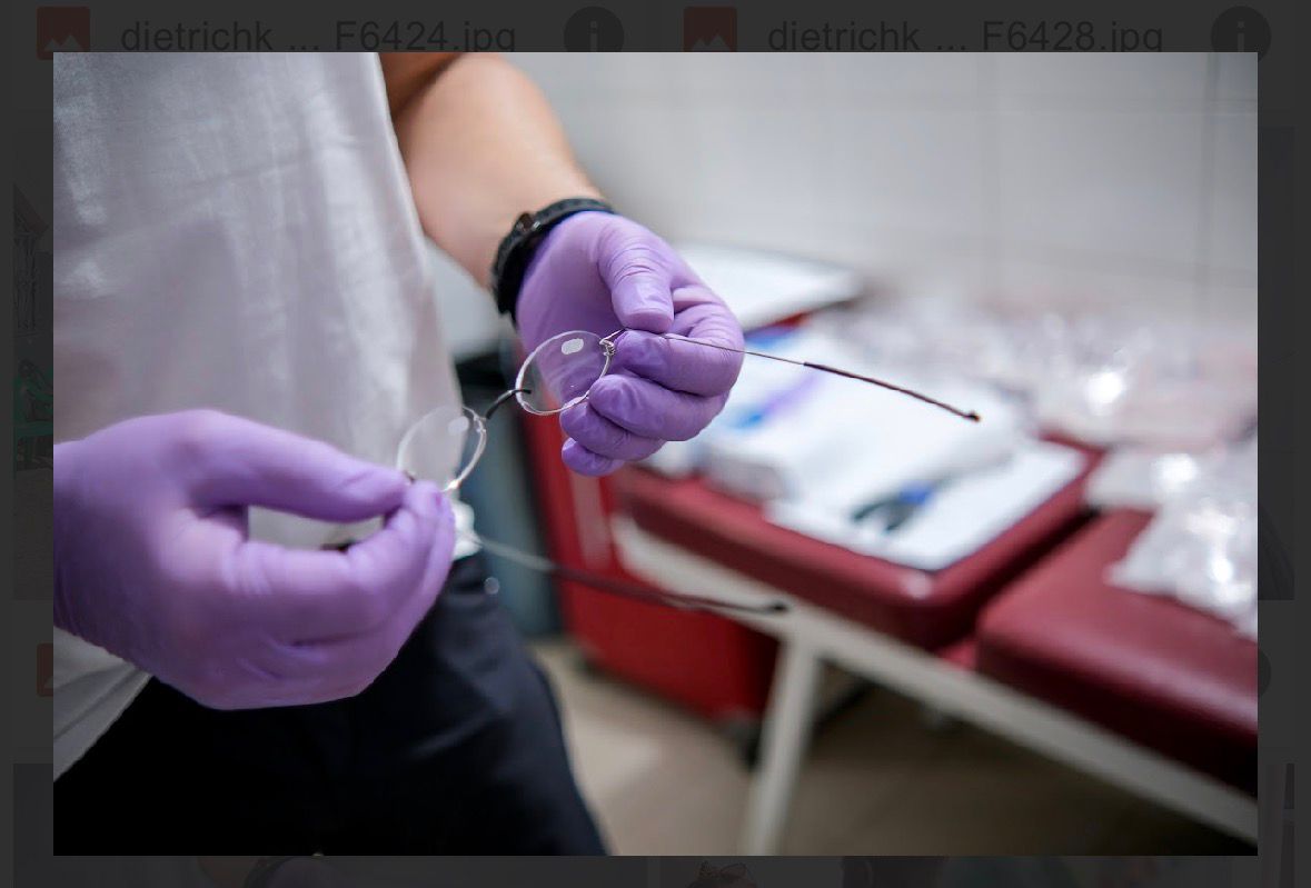 Behandschuhte Hände halten eine Brille zur Anpassung